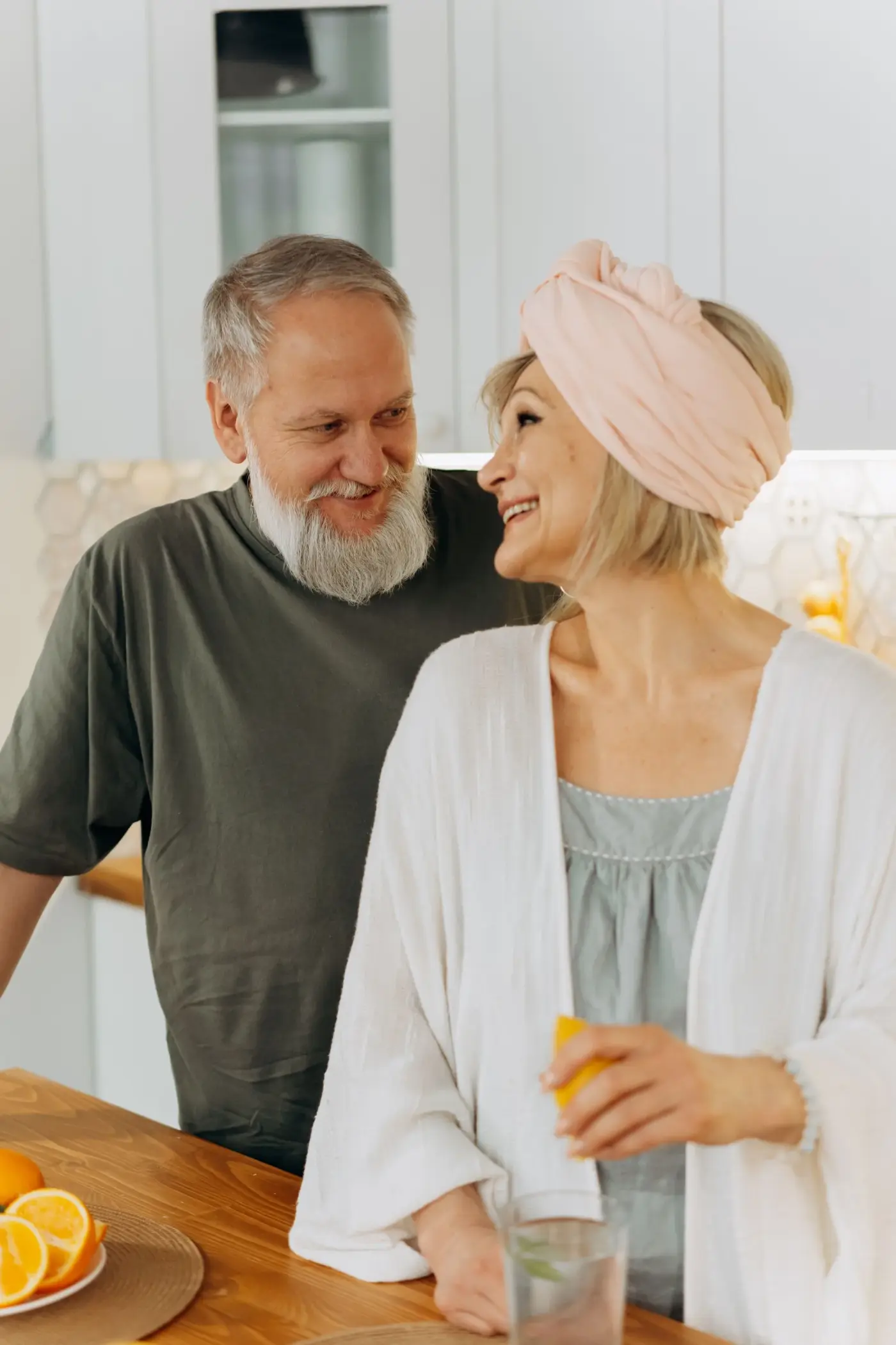 An older couple standing in a kitchen, smiling at one another