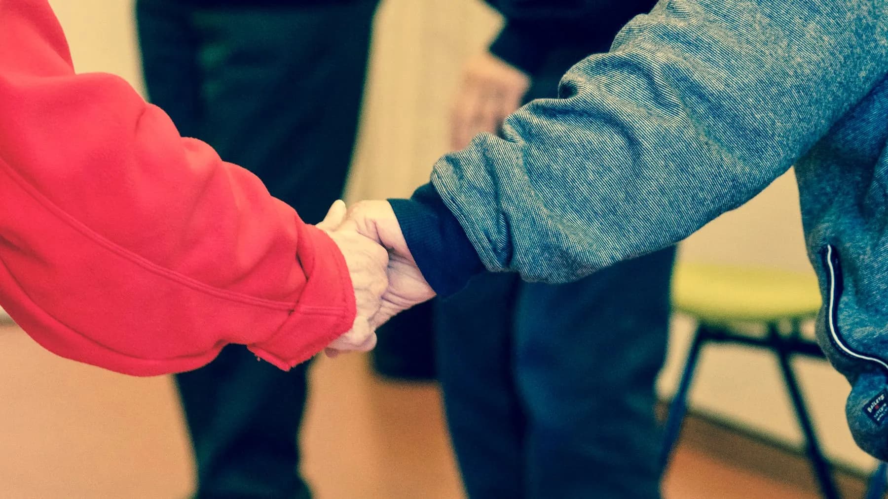 Two people holding hands, one wearing a red sleeve, the other denim