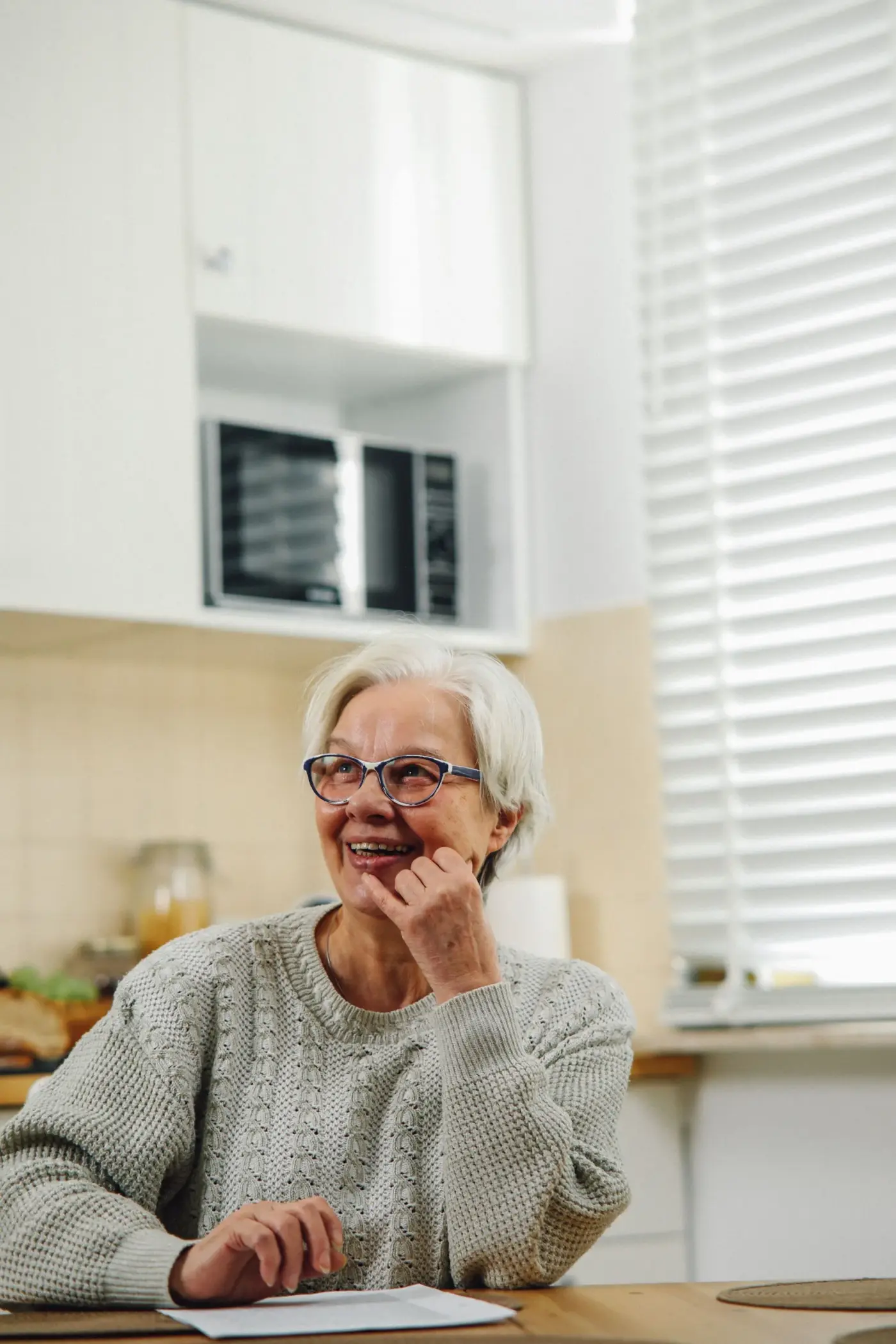 An older woman smiling by a bright kitchen window