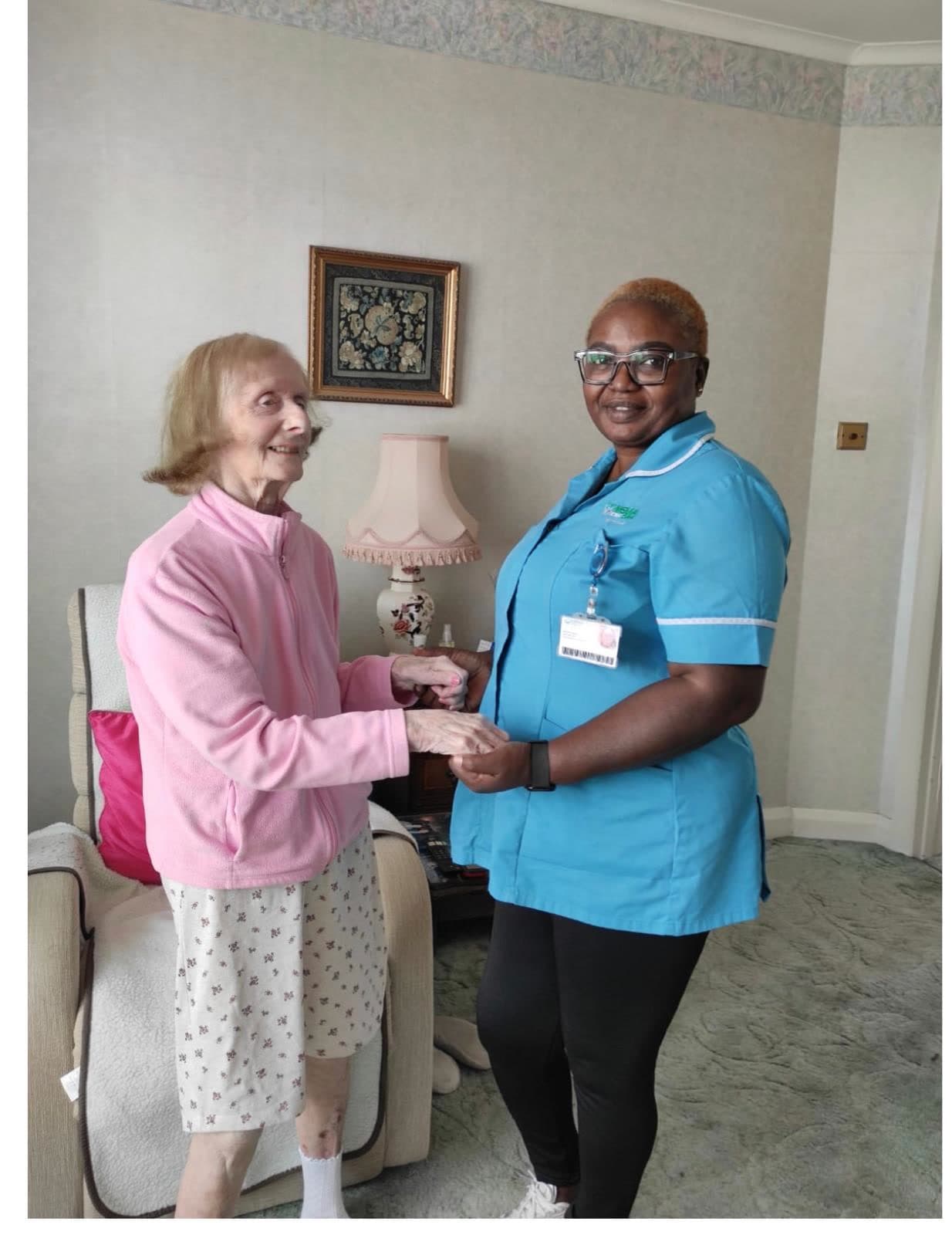 A Nema carer in uniform holding hands with an older woman in her living room